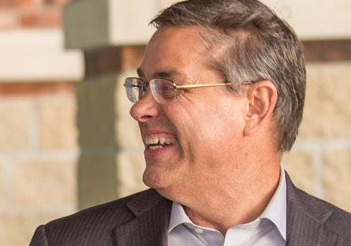 A man with glasses and a suit smiling.