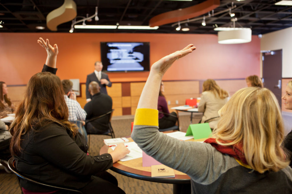 A group of people sitting at tables with their hands raised.
