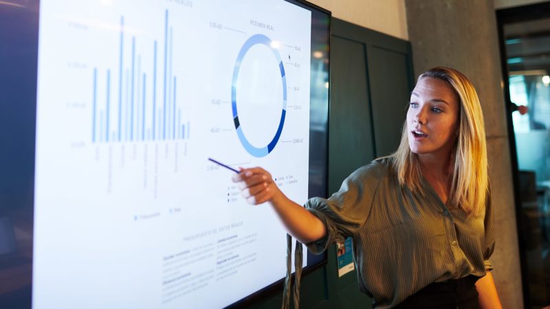 A woman is pointing to a chart on the screen.