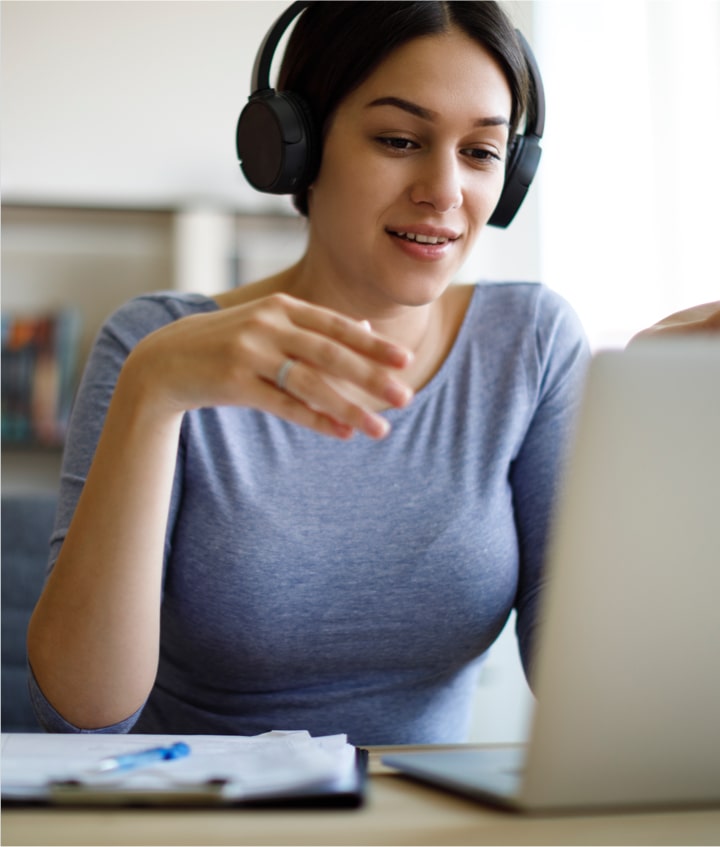 A woman wearing headphones while looking at her laptop.