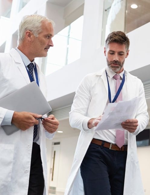 Two doctors are standing in a building looking at papers.